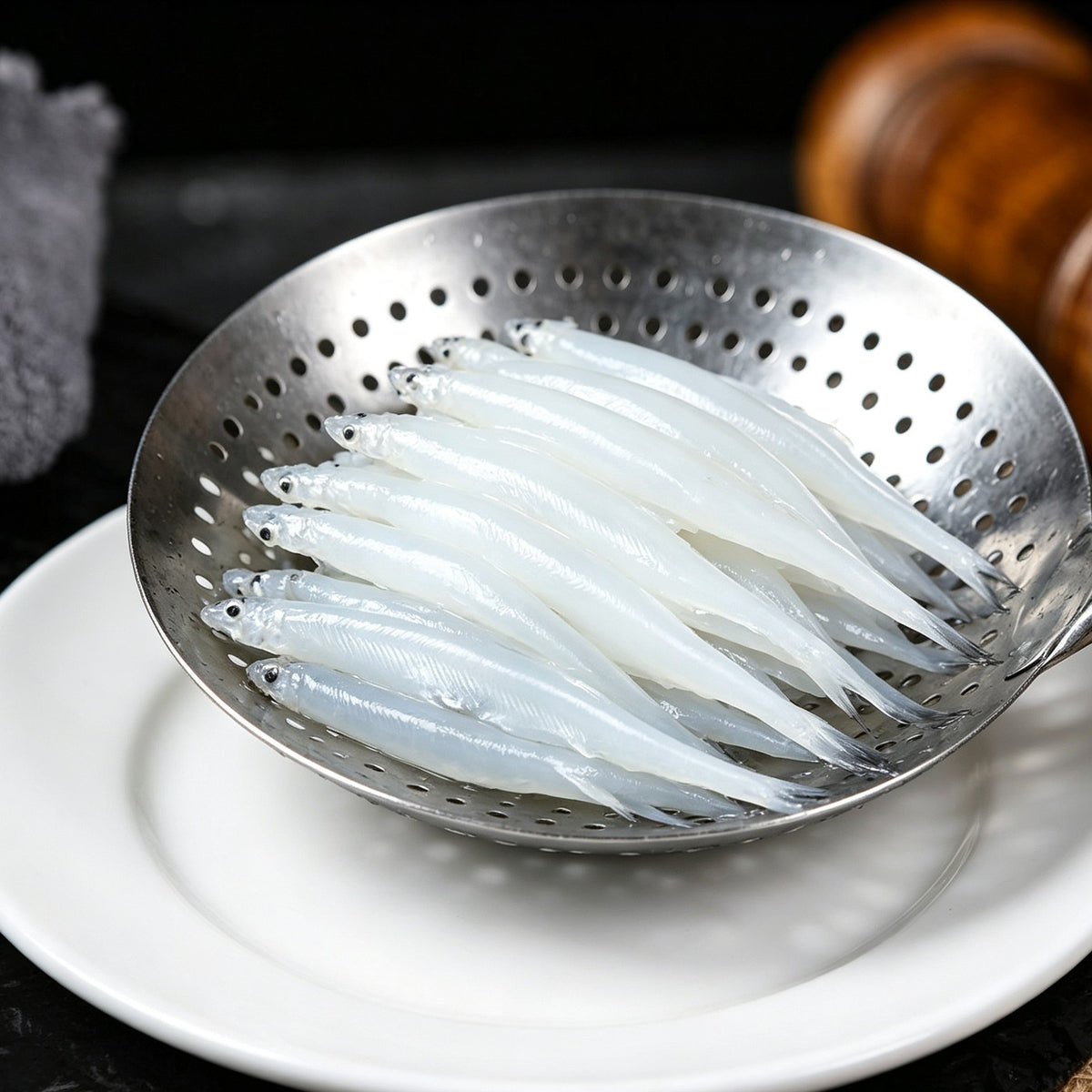 Whitebait drained in a metal colander over a white plate
